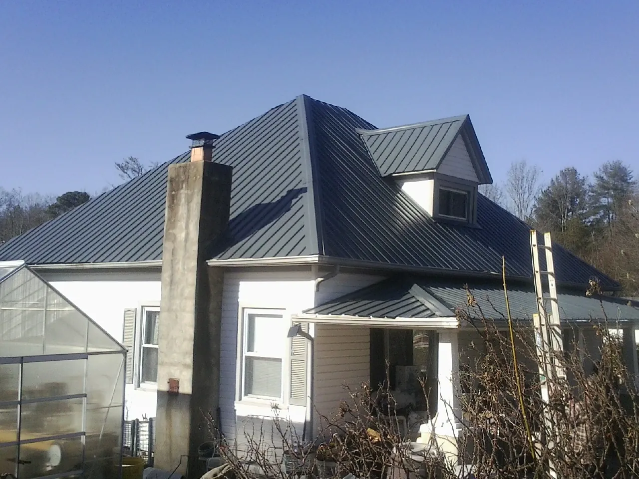 Dark blue standing seam metal roof on a white farmhouse with dormer in Demotte