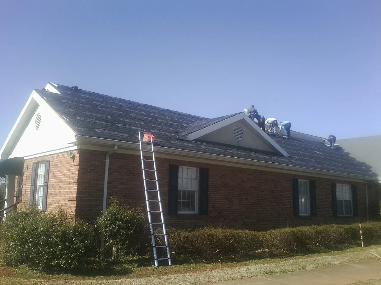 Crew tearing shingles off a brick ranch roof with a ladder set — Emergency Roof Repair work by our crew in Demotte