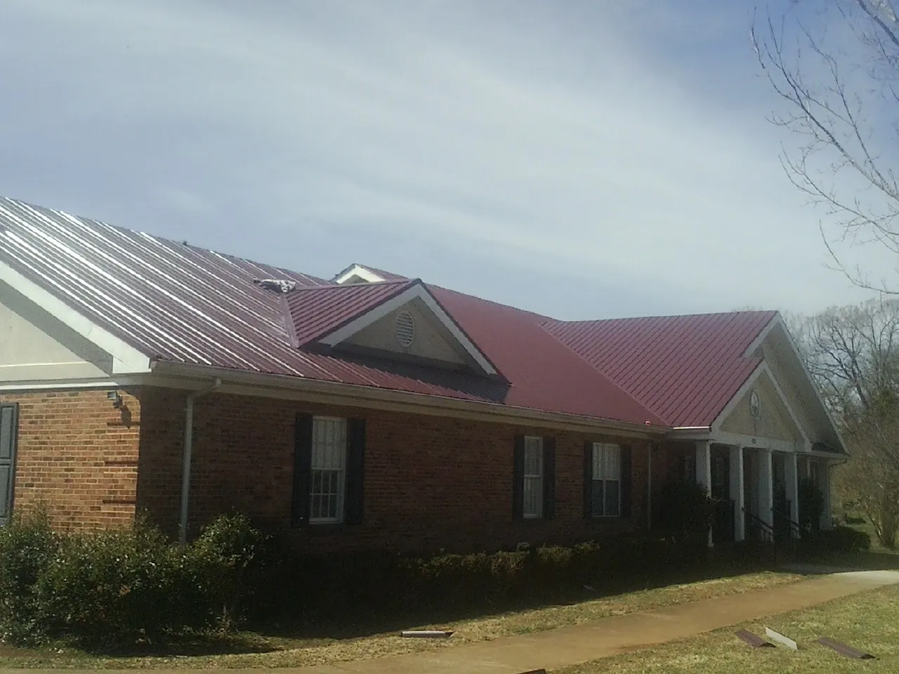 Red metal roof with gabled entries on a long brick building, from a Hail Damage Roof Repair job in Demotte