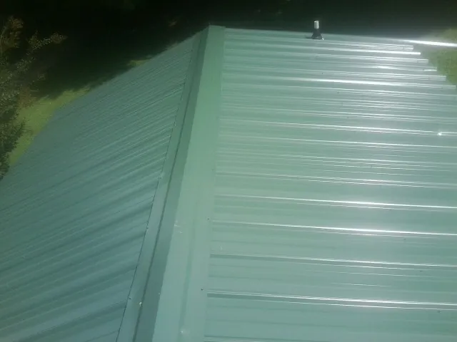 New green metal panels meeting at the ridge of a roof — Flat Roof Repair work by our crew in Demotte