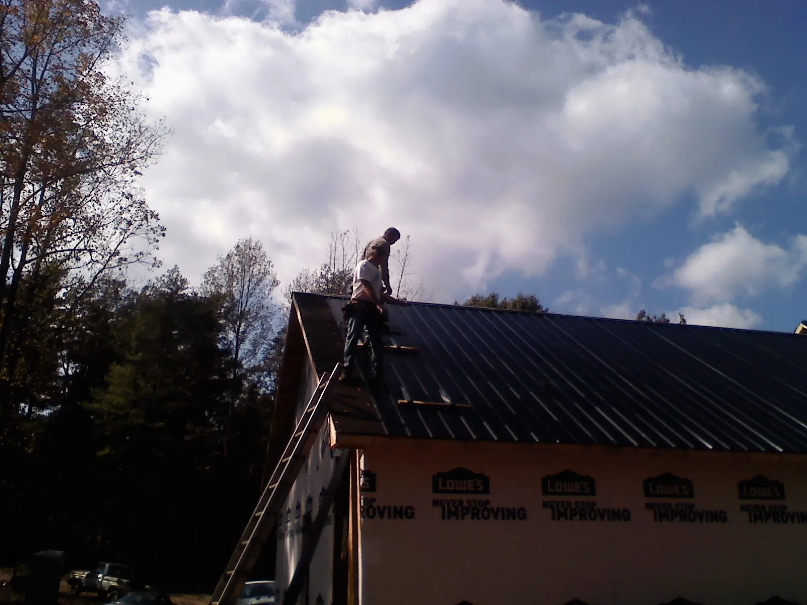 Roofer fastening dark metal panels high against a cloudy sky, from a Roof Inspection job in Demotte