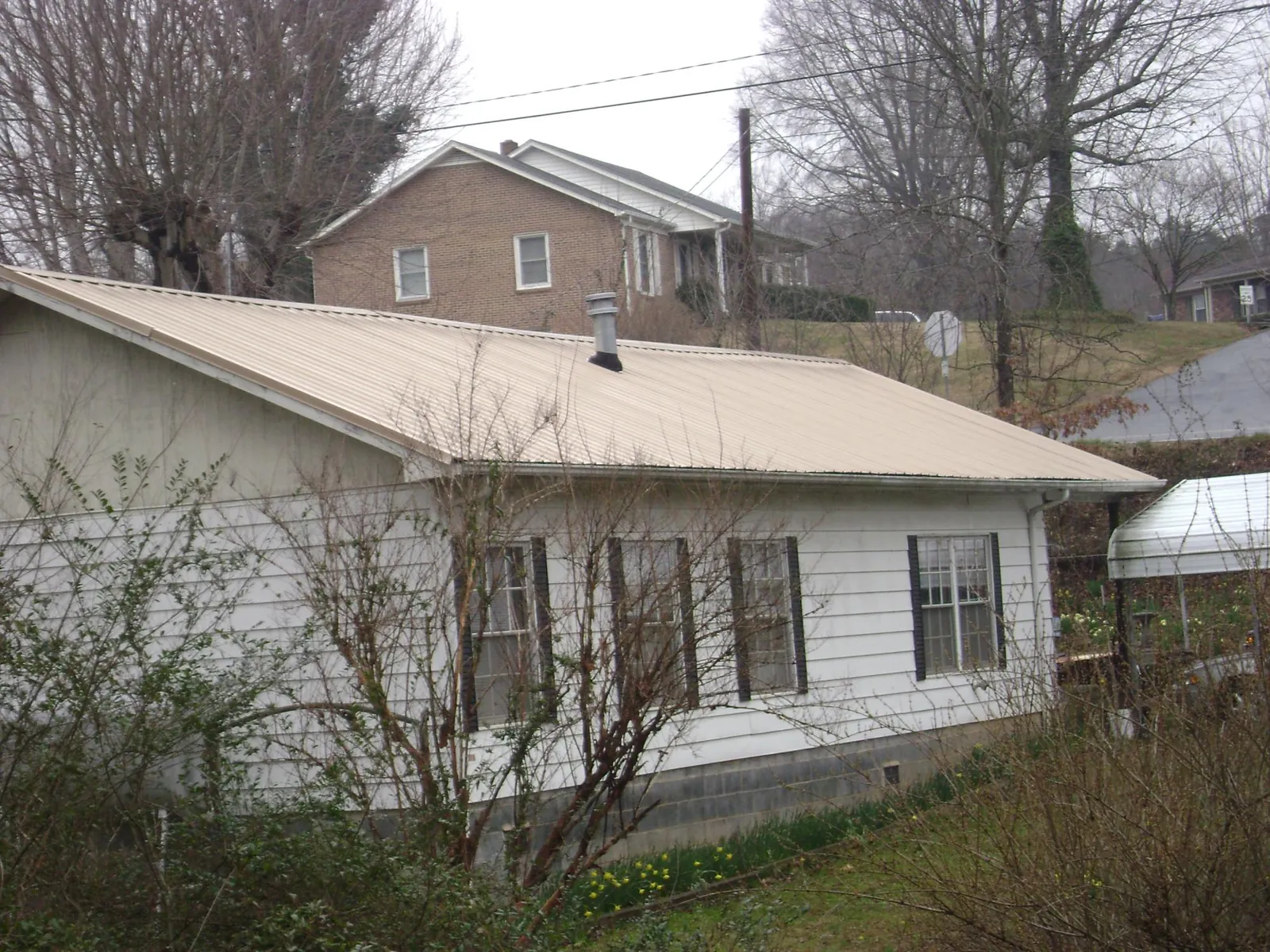 Tan metal roof on a white sided house set into a hillside — Commercial Roofing by Roofing Brothers in Demotte