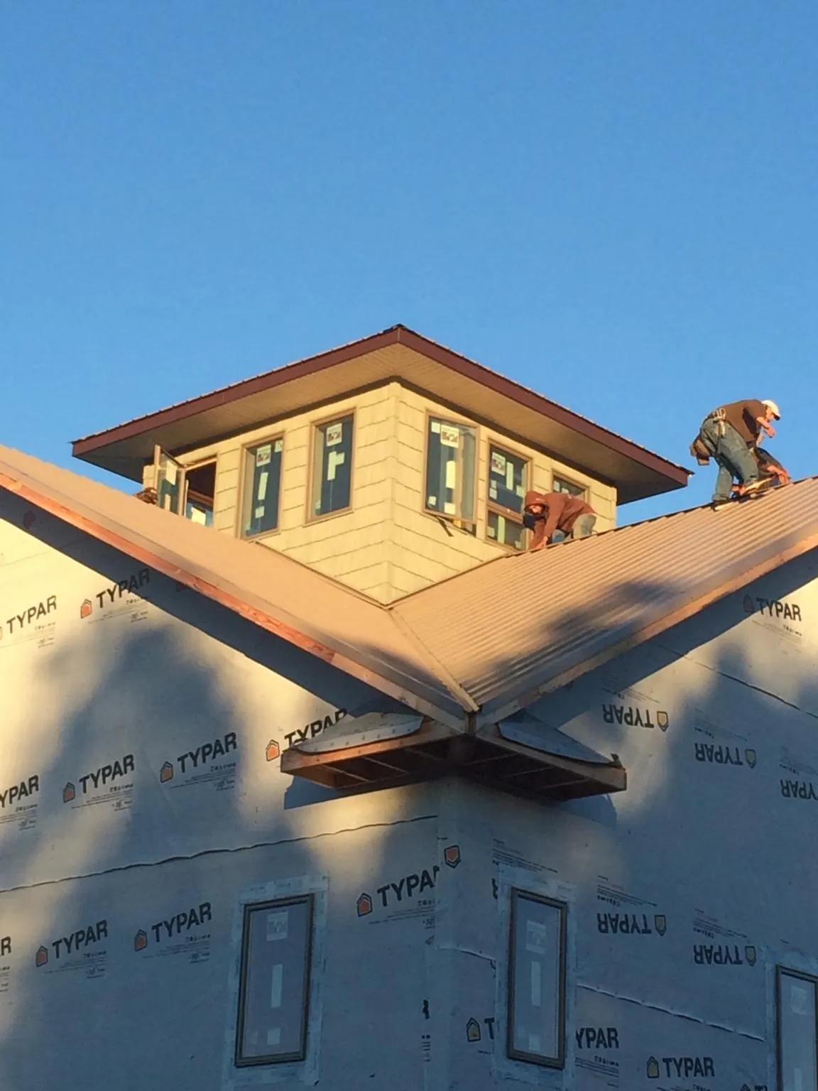 Roofers working around a rooftop cupola on a new metal roof at sunset — Roof Waterproofing in Demotte by Roofing Brothers
